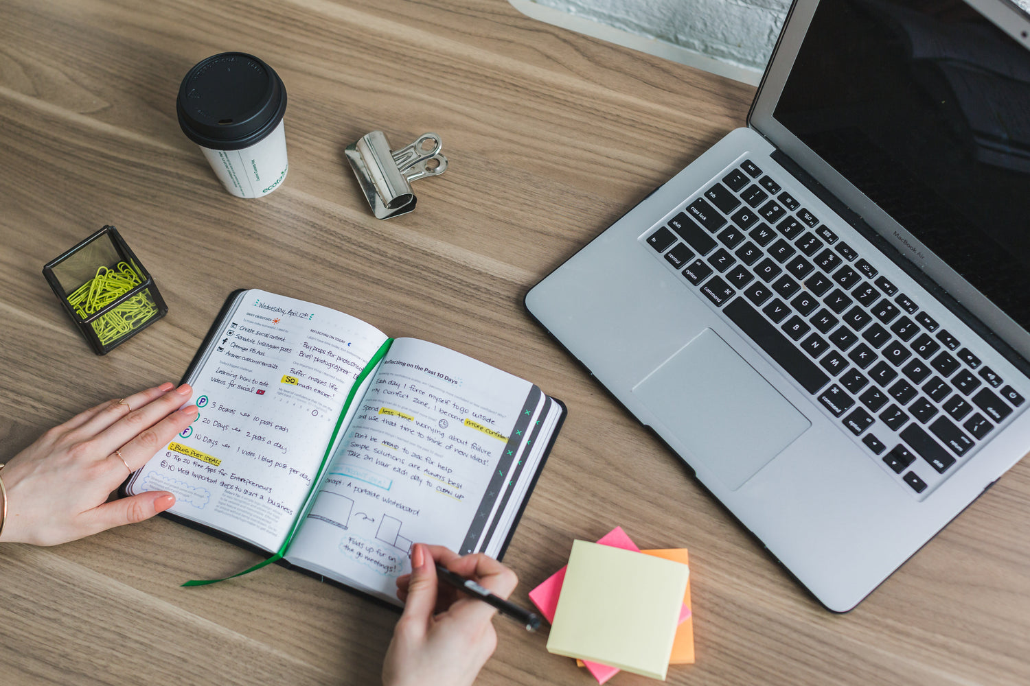 Fernstudentin schreibt am Mac an einer Hausarbeit, Notizbuch und Kaffee auf dem Schreibtisch